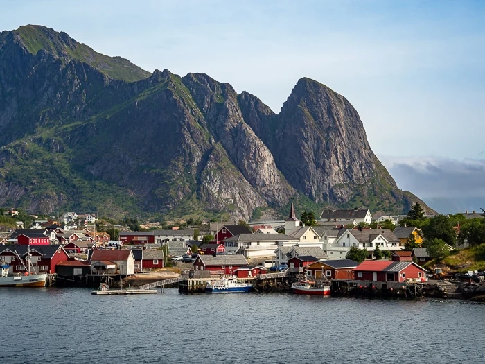 Small white and red wooden buildings with a backdrop of a large granite mountain at Reine