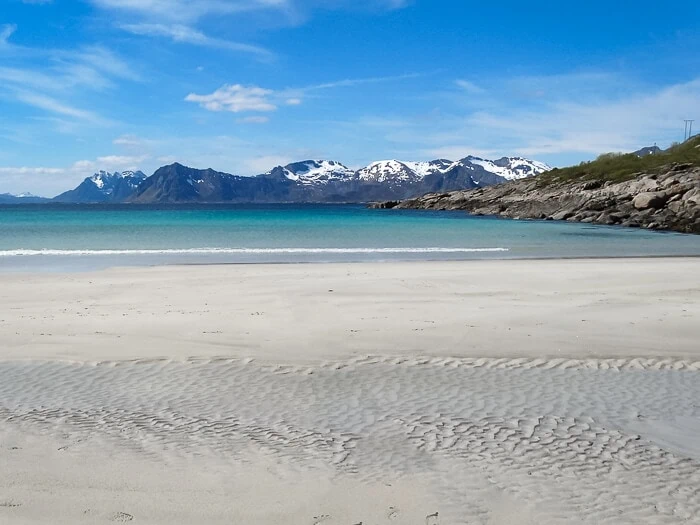 a big patch of white sand and a view of snow-capped mountains in the distance at Rørvik Beach, a popular place for swimming in Lofoten
