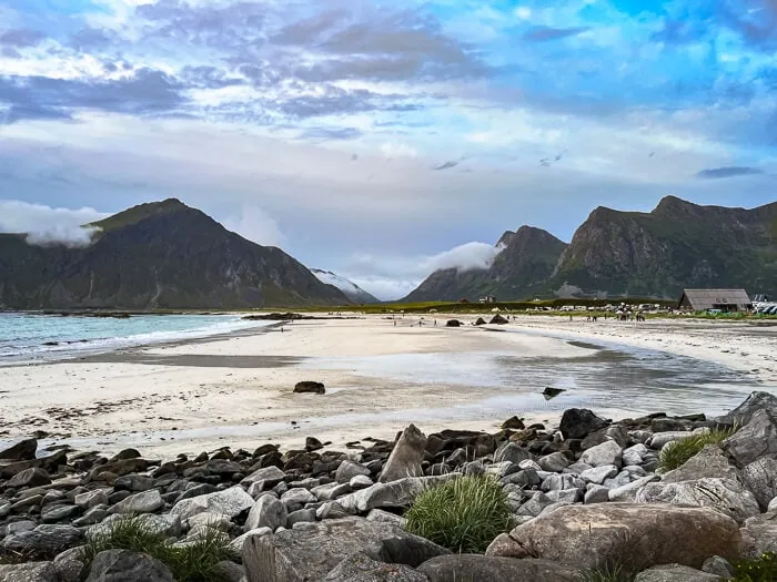 Cloudy sky, mountainous landscape and a wide stretch of white sand at Skagsanden Beach, one of the best places for surfing in Lofoten