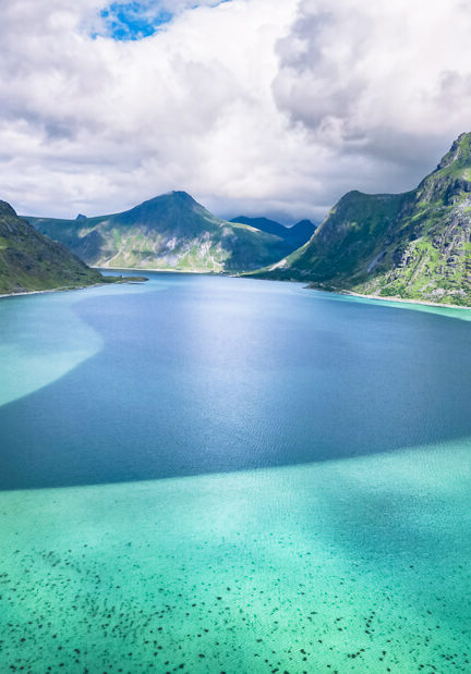 Neon blue sea surrounded by green mountains at Flakstadpollen in Lofoten