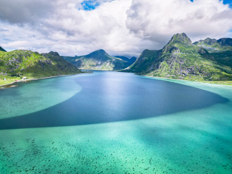 Neon blue sea surrounded by green mountains at Flakstadpollen in Lofoten