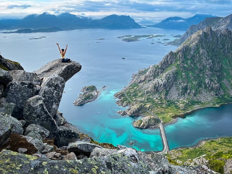 A woman sitting on a slab of rock protruding from a mountainside at Torsketunga, one of the top hikes in Lofoten