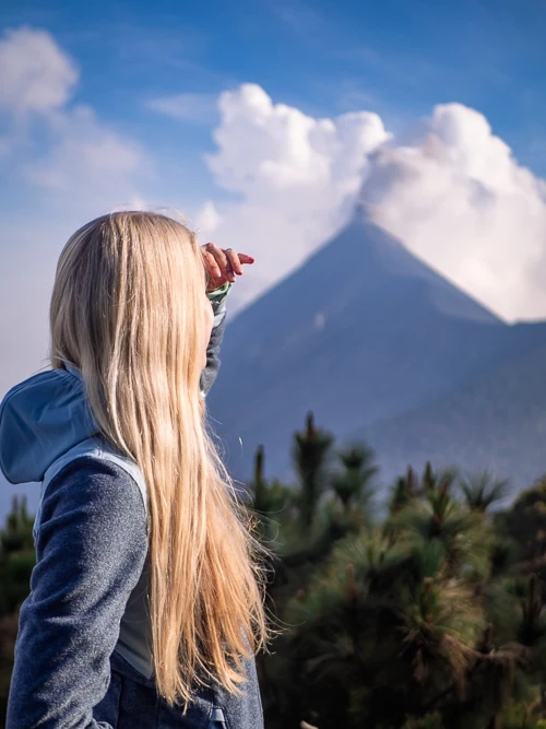 a woman looking at Volcan Fuego blowing out smoke in the distance