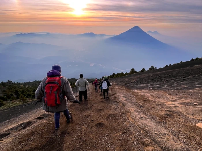 Hikers trekking down the side of Acatenango Volcano with panoramic views of Guatemalan highlands in the background