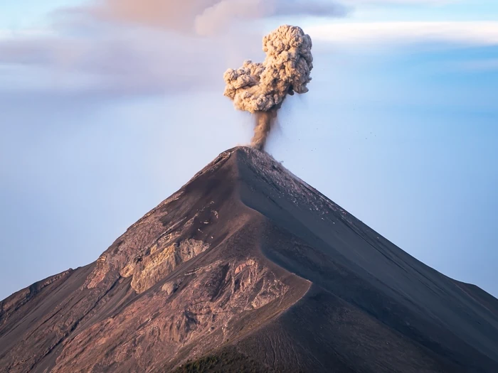 A plume of grey smoke bursting out of the crater of Volcan Fuego during sunrise