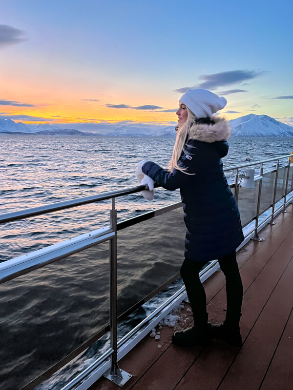 Me standing on the deck of our whale safari boat with mountains and orange sky in the background