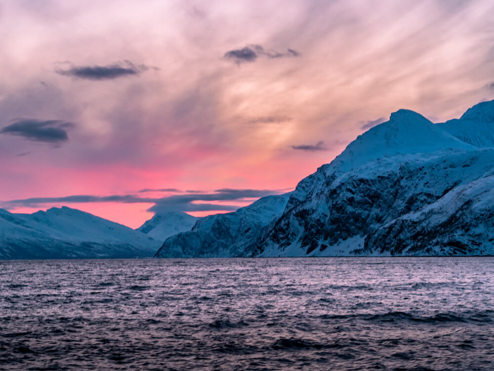 A view of snow-covered mountains against pink and orange sky on our whale tour from Tromso.