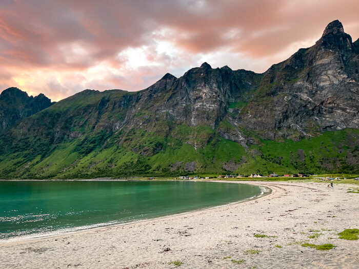 an empty white sand beach with emerald water, surrounded by dramatic mountains at Ersfjord Beach, one of the best places for camping in Senja