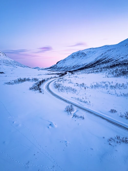 Snow-covered valley surrounded by mountains and pastel-colored sky on Kvaløya island during the blue hour