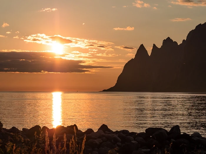 orange sky and the Midnight Sun next to steep pointy mountains on the coast of Senja Island, Norway