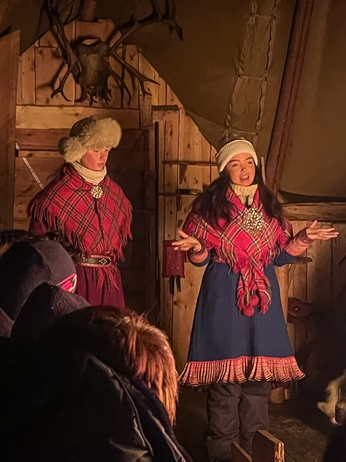 Two Sami girls in traditional Sami clothing sharing stories about their culture and traditions to visitors