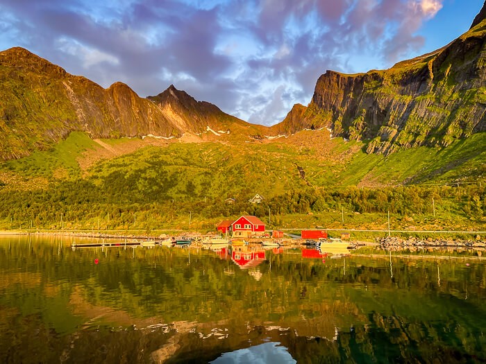 A small red fisherman cabin on the edge of a fjord with a lush green mountain range in the background near Ersfjordstranda