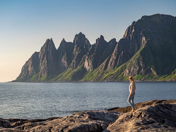Me standing on a rocky beach with a backdrop of steep jagged mountains on Senja Island, Norway