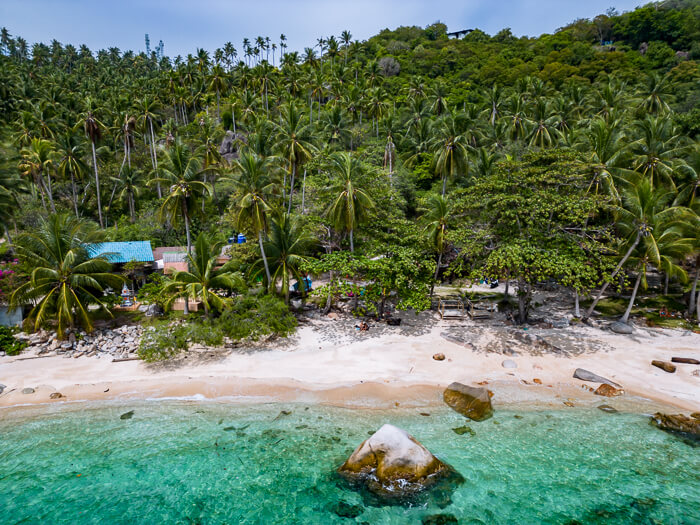 A drone photo of June Juea Beach with its turquoise water, white sand and countless palm trees, one of the more hidden beaches of Koh Tao.