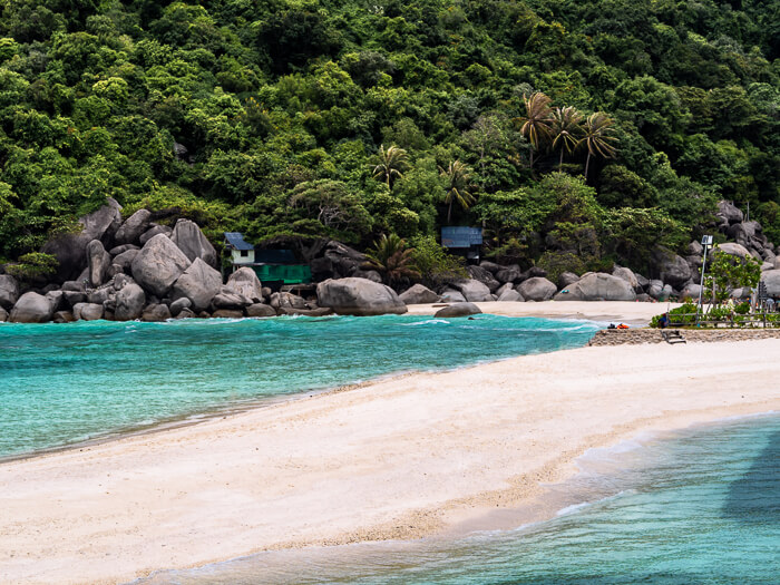 A long narrow sandbank bordered by clear blue water on both sides and lush forest in the background.