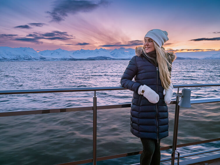 Me standing on the deck of a whale watching tour boat with snowy mountains and pastel-colored sky in the background.