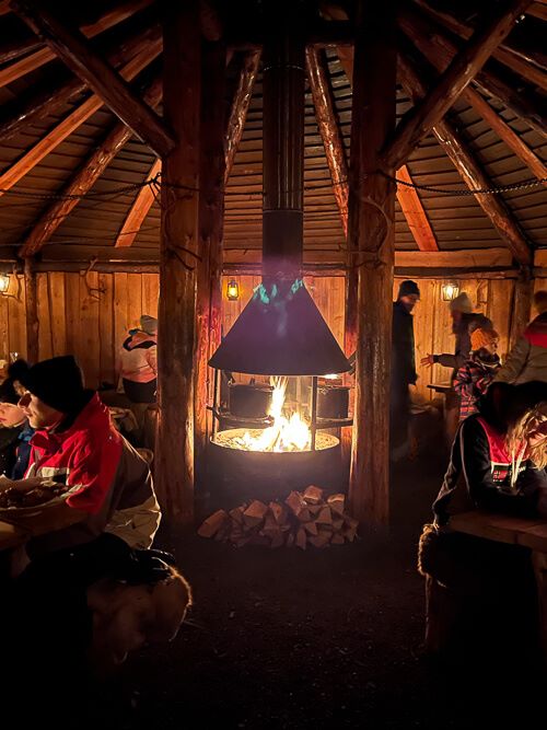 People having dinner around a fire in a wooden Sami hut.