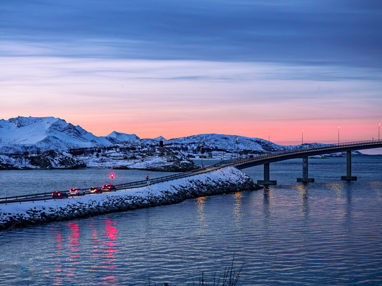 Pink skies, snowy mountains and a bridge near Sommaroy island during the twilight hours of the Polar Night period in December in Tromso.