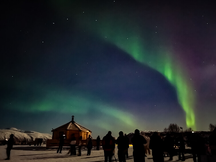 People admiring and photographing green and purple Northern Lights outside Tromso.