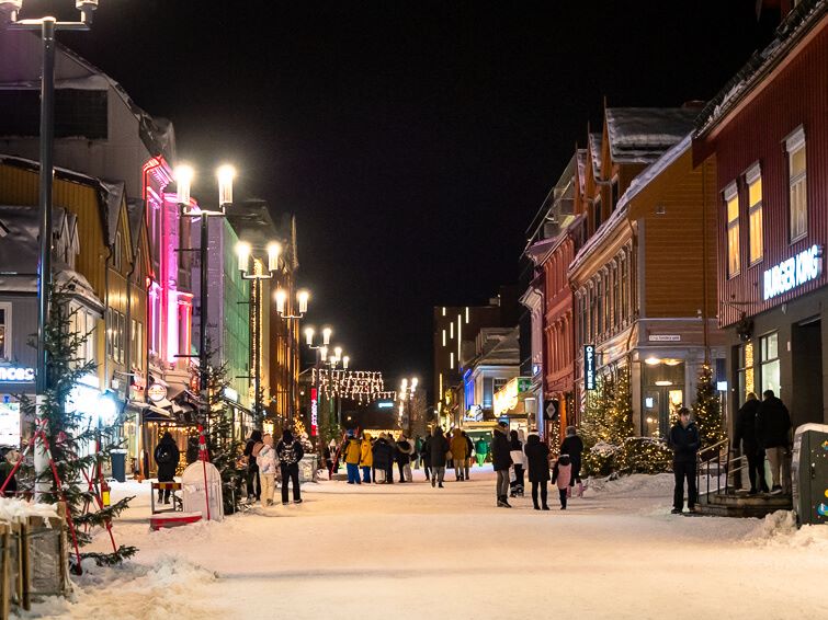 Pedestrians walking along the Storgata shopping street lined with wooden houses and Christmas lights in the center of Tromso in December.