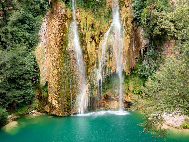 The tall Cascade de Sillans waterfall surrounded by lush vegetation and a basin with emerald water below it.