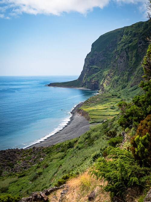 The rocky beach of Faja de Lopo Vaz bordered by Atlantic Ocean on one side and steep green cliffs on the other.