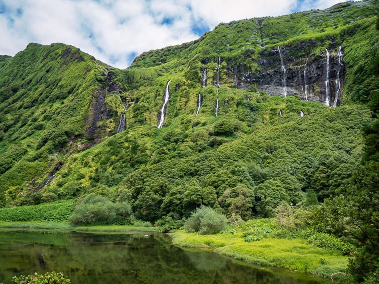 Multiple streams of water trickling down a steep mountainside covered with lush vegetation at Ribeira do Ferreiro waterfalls.