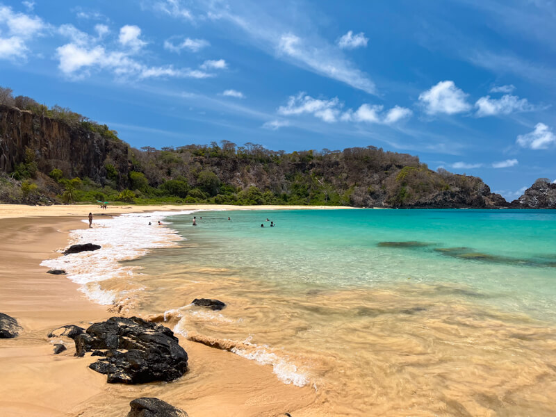 Calm blue-green water and golden sand with a backdrop of steep cliffs at Sancho Bay, the most iconic beach in Fernando de Noronha.