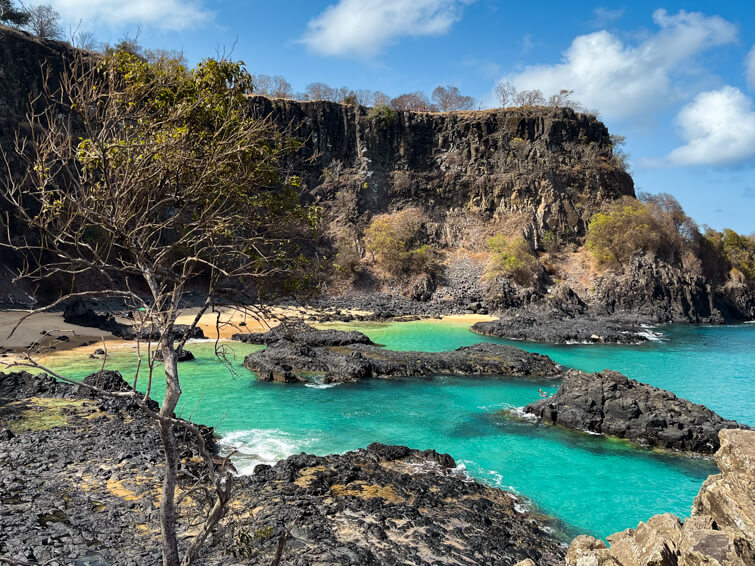 Neon blue water and black volcanic rocks at Baia dos Porcos, one of the best places to visit in Fernando de Noronha.