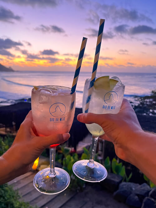 Two cocktails with colorful sunset sky in the background at Bar do Meio, one of the best restaurants in Fernando de Noronha.