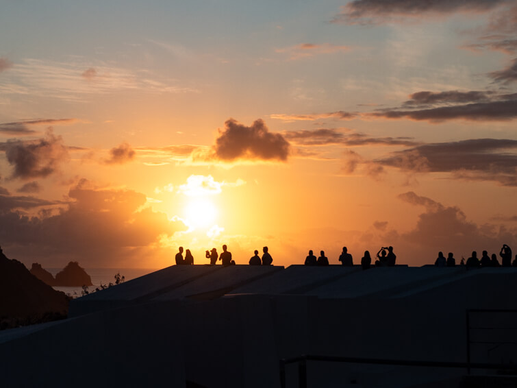 A group of people admiring the sunset at a viewing platform at Forte Noronha with orange sky in the background.