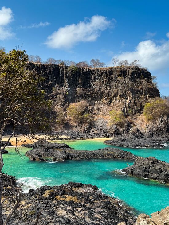 Neon blue water and black volcanic rocks at Baia dos Porcos, one of the best places to visit in Fernando de Noronha.