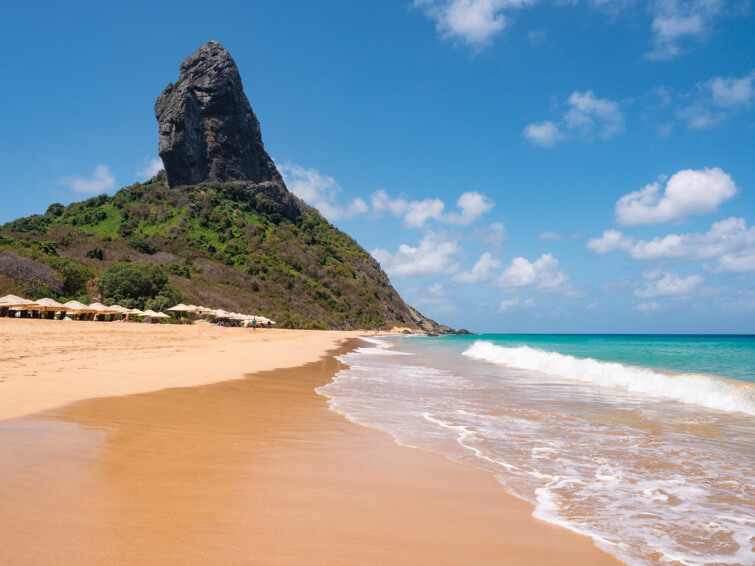 A stretch of golden sand, bright blue ocean and a view of the Morro do Pico mountain at Conceição Beach, one of the best beaches in Noronha.