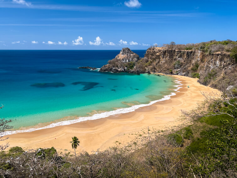 The crescent-shaped Sancho Beach with golden sand and pristine blue-green water on a sunny day.