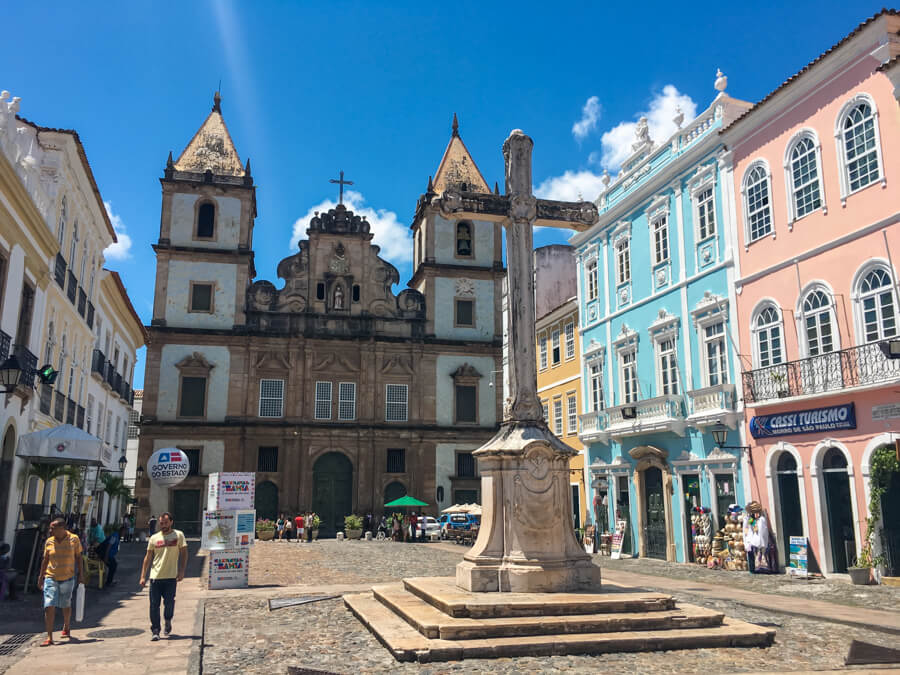 A square surrounded by pastel colored buildings with intricate facades and a church with colonial architecture in Salvador de Bahia.