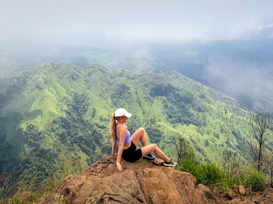 Me sitting on the ground overlooking a green valley on the Ella Rock hike, one of the best things to do in Ella.