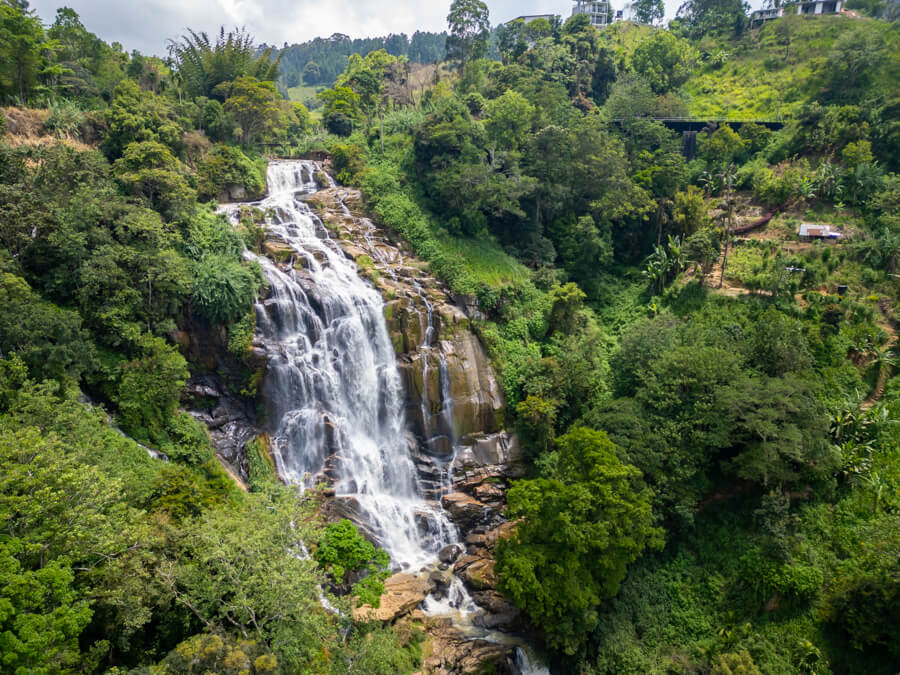 An aerial drone photo of the cascading waters of Small Ravana Falls surrounded by green vegetation.