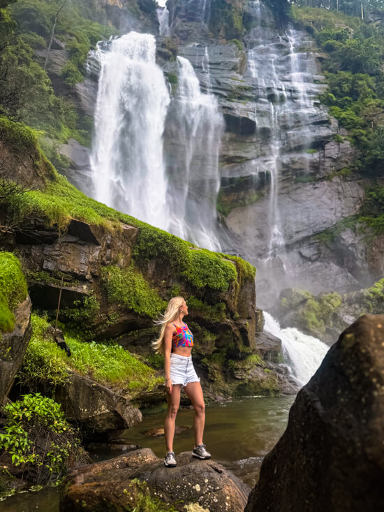 Me standing on a rock in front of the white cascading waters of Bomburu Ella waterfall.