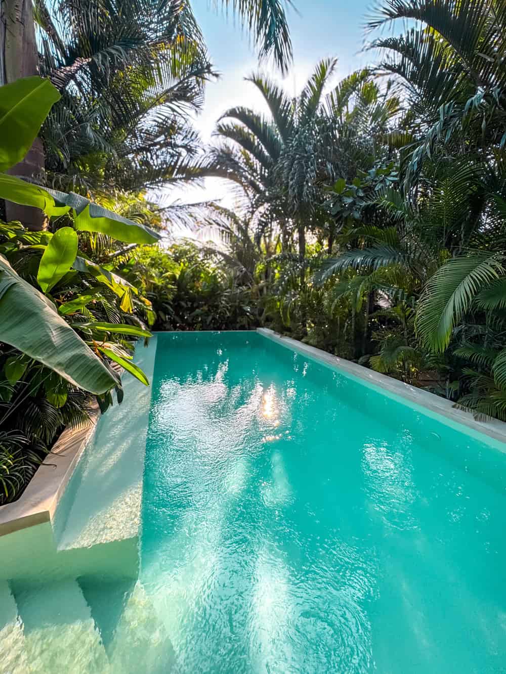 A pool with turquoise water surrounded by lush tropical greenery at Gaia Villas Hotel in Nungwi.