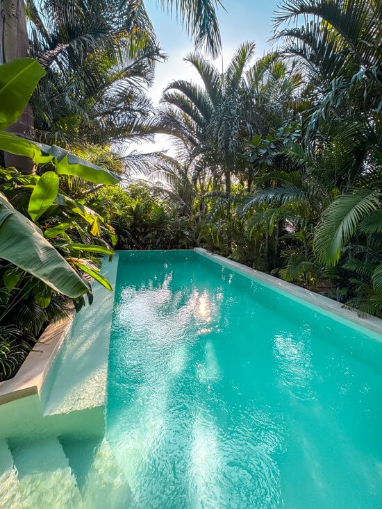 A pool with turquoise water surrounded by lush tropical greenery at Gaia Villas Hotel in Nungwi.