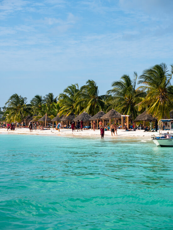 Turquoise sea and a busy white sand beach lined with palm trees and parasols in Kendwa, Zanzibar.