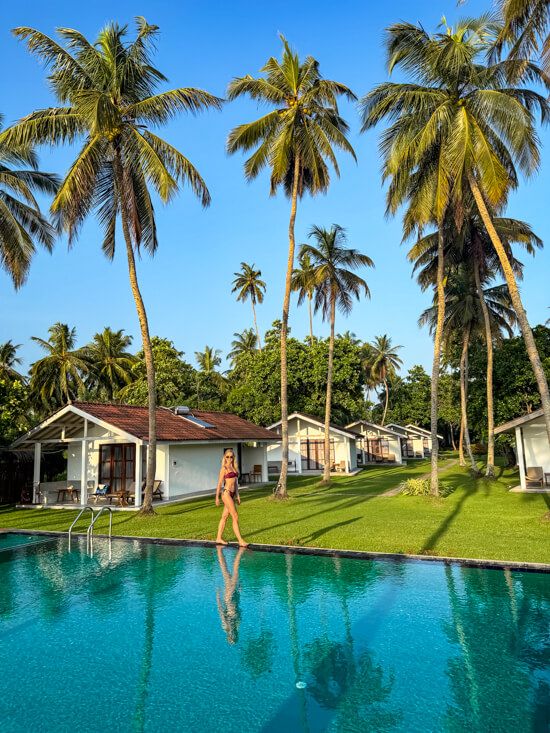 Me walking along the edge of a pool in our hotel in Tangalle with tall palm trees and bungalows in the background.