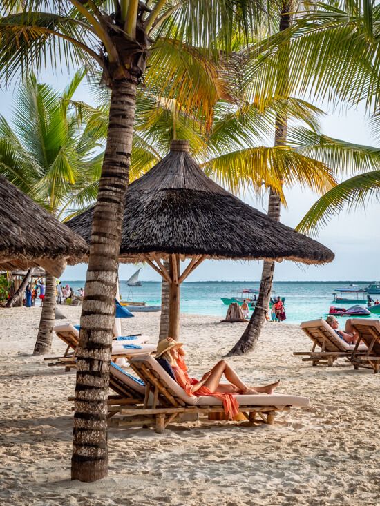 Me lying on a sunbed underneath a large parasol made of straw on a white sand beach at Zuri Zanzibar.