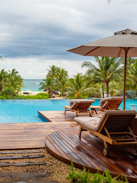 Sunbeds next to a bright blue infinity pool with palm trees in the background.