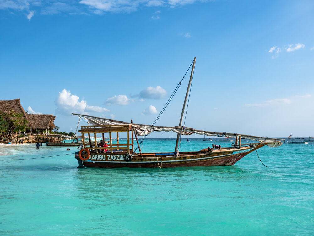 A traditional wooden dhow boat in bright turquoise sea at Nungwi Beach. 