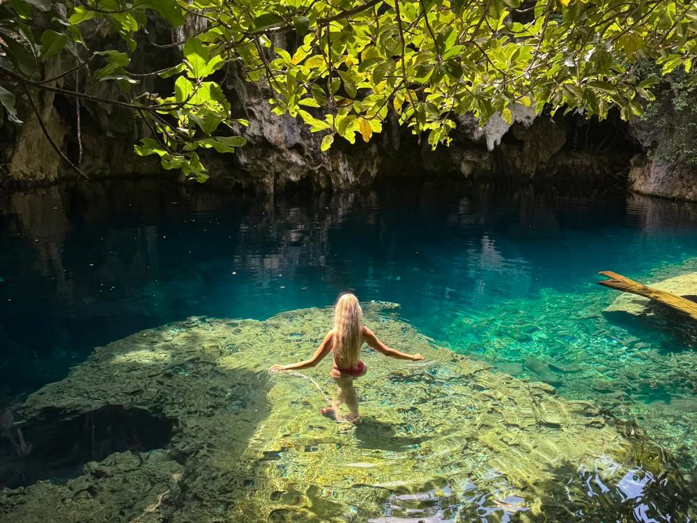 Me standing in shallow crystal clear water surrounded by rock walls and vegetation at Maalum Cave.