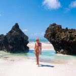 Me standing in front of two black rock formations surrounded by white sand at Mtende Beach, Zanzibar.