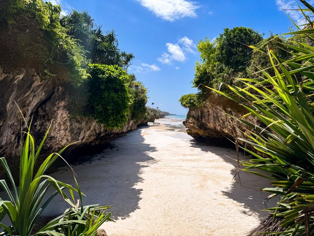 Mtende Beach with its narrow stretch of sand between two cliffs, with lush green vegetation growing on top of them.