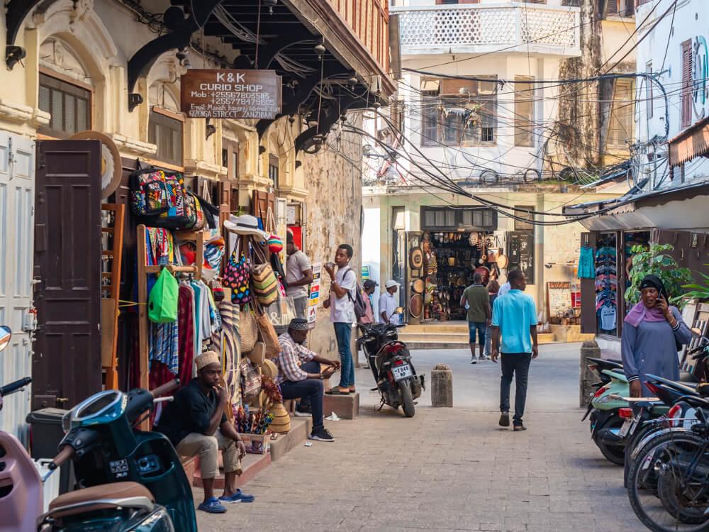 A walking street lined with souvenir shops and buildings with historical architecture in Stone Town.