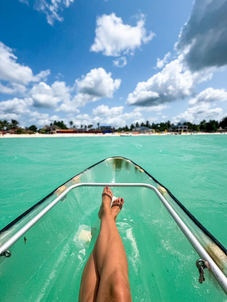 My legs in a transparent kayak surrounded by vibrant blue water at Paje Beach.